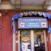 Il negozio si affaccia sulla strada. Sulla porta a vetri sono affissi i manifesti della compagnia telefonica rumena e linsegna blu con la scritta in italiano salumeria e il nome Ca la mama acasa  prodotti tipici rumeni
